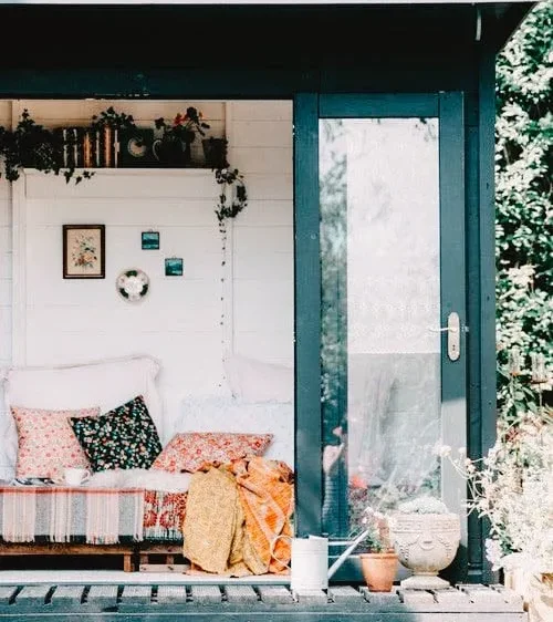 She Shed with a bohemian decor, featuring a cozy couch with colorful cushions, hanging plants, and a glass door, set in a lush garden.