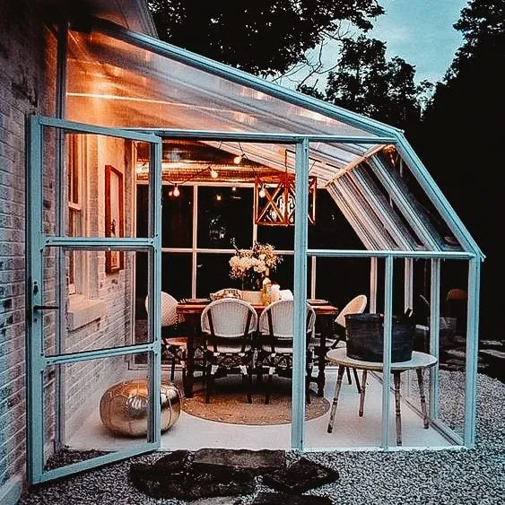 Cozy glass sunroom attached to home, illuminated at dusk with warm lighting and comfortable seating