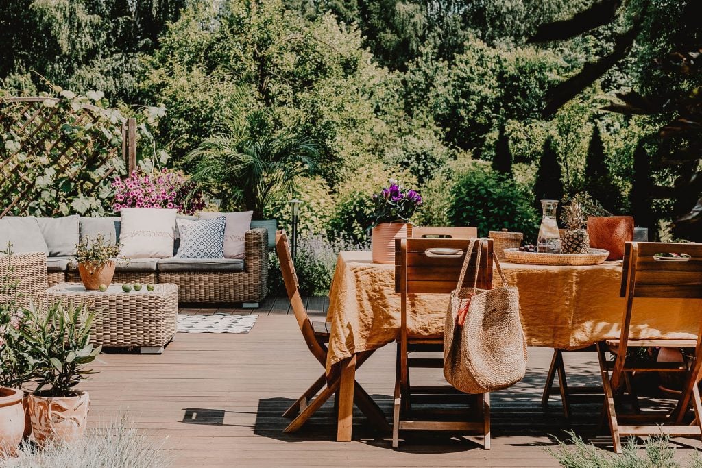 Wooden chairs at Dining table covered with orange tablecloth standing on wooden deck in green garden