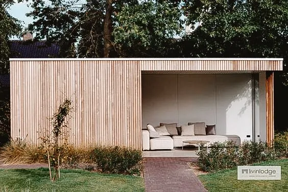 Abri de jardin moderne avec des lattes en bois et un espace salon ouvert, entouré d'un jardin bien entretenu et de verdure.