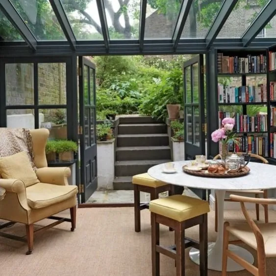 Solarium élégant avec toit en verre, bibliothèque, et mobilier confortable donnant sur un jardin verdoyant.