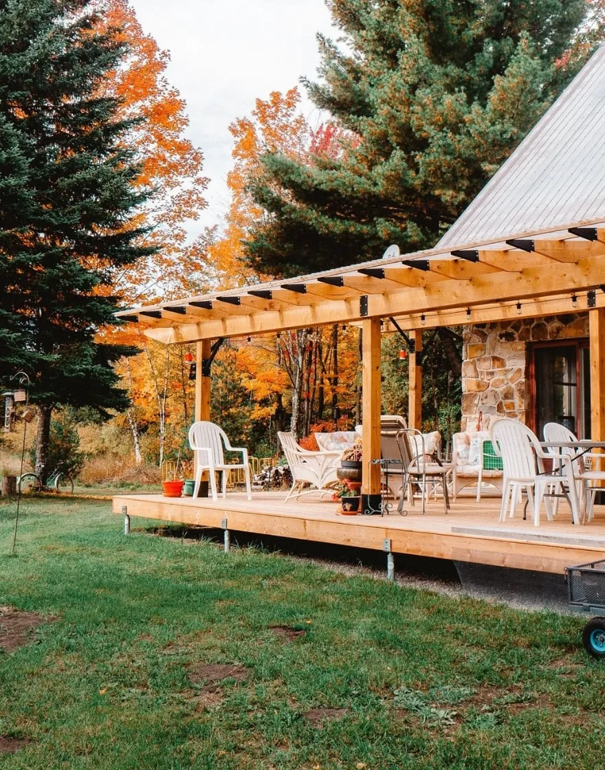 Wooden deck with pergola surrounded by autumn trees.