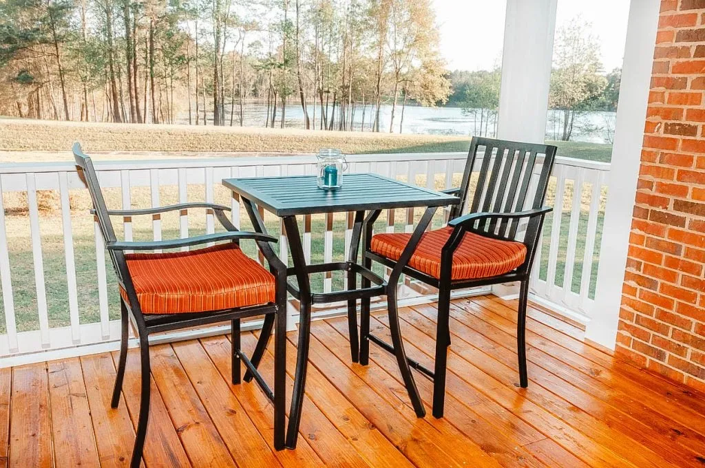 Un coin repas sur une terrasse avec une table et des chaises, offrant une vue sur un paysage verdoyant et un plan d'eau en arrière-plan.