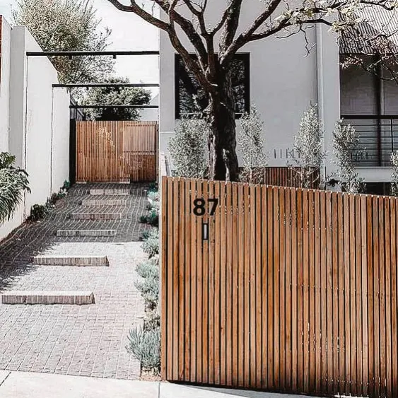 Modern wooden fence in front of a house with a paved walkway.