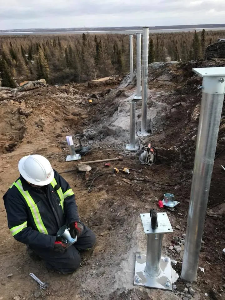 Worker installing screw piles on rocky terrain for foundation